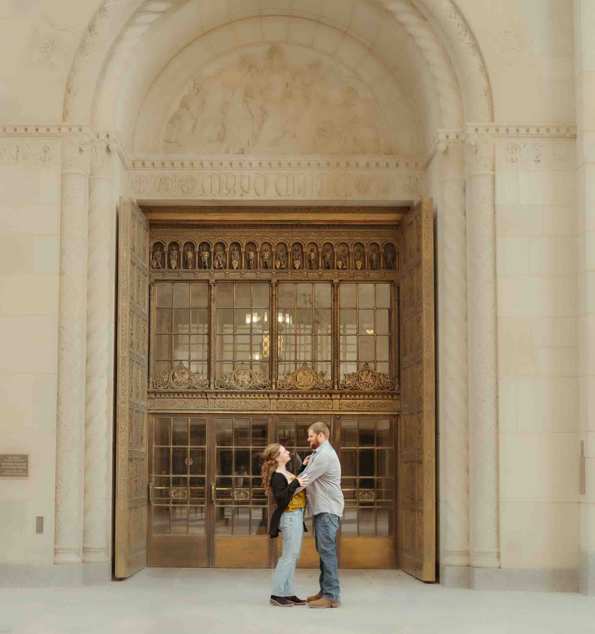 couple hold each other and standing in front of copper doors downtown Rochester mn