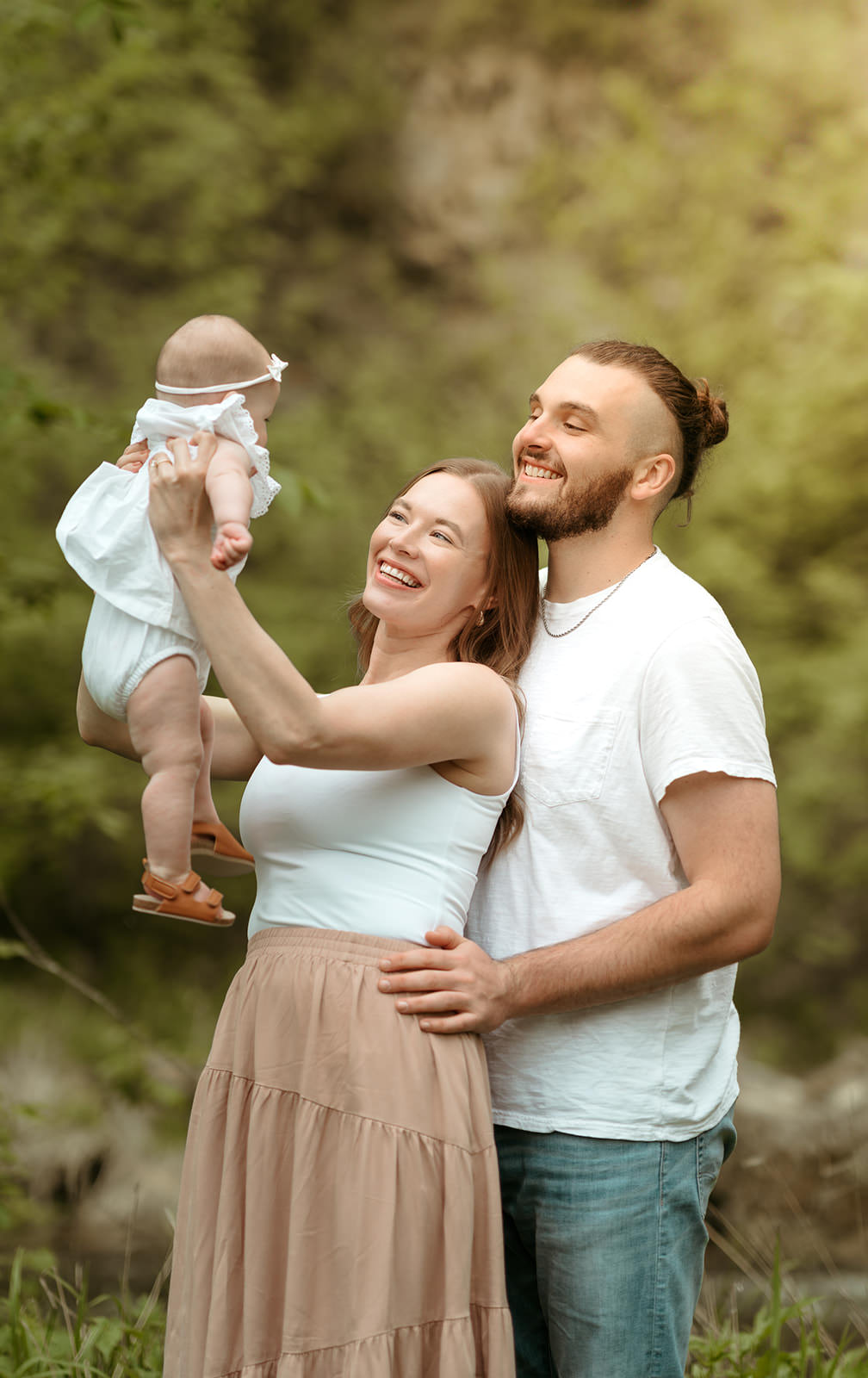mom holding baby up with dad standing behind her.
